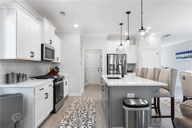 kitchen featuring appliances with stainless steel finishes, a breakfast bar, decorative light fixtures, white cabinetry, and a center island with sink