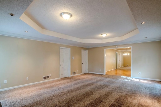 empty room with a textured ceiling, crown molding, a raised ceiling, and light carpet