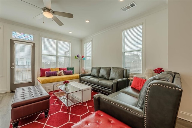 living room with visible vents, ornamental molding, wood finished floors, baseboards, and ceiling fan