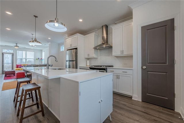 kitchen with backsplash, appliances with stainless steel finishes, white cabinetry, wall chimney exhaust hood, and a sink