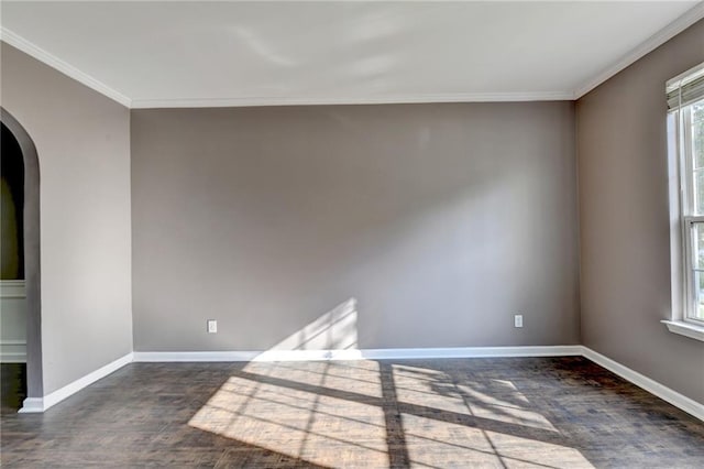 empty room with baseboards, arched walkways, dark wood finished floors, and crown molding