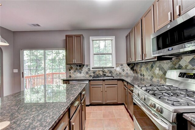 kitchen with backsplash, appliances with stainless steel finishes, light tile patterned floors, sink, and dark stone countertops