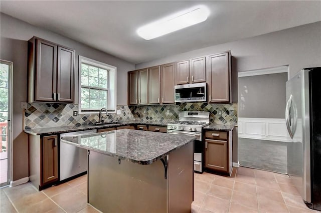 kitchen featuring light tile patterned floors, appliances with stainless steel finishes, dark stone countertops, a center island, and a sink