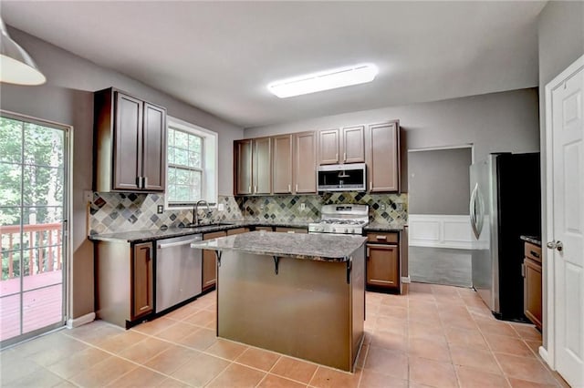 kitchen featuring tasteful backsplash, dark stone countertops, a center island, stainless steel appliances, and a sink