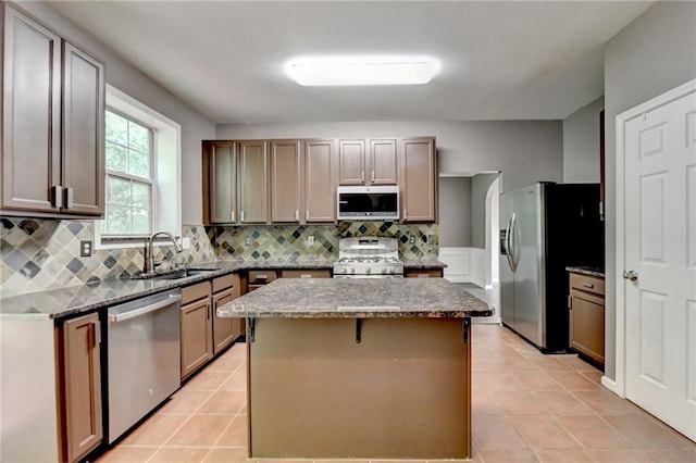 kitchen with a center island, decorative backsplash, appliances with stainless steel finishes, light tile patterned flooring, and a sink