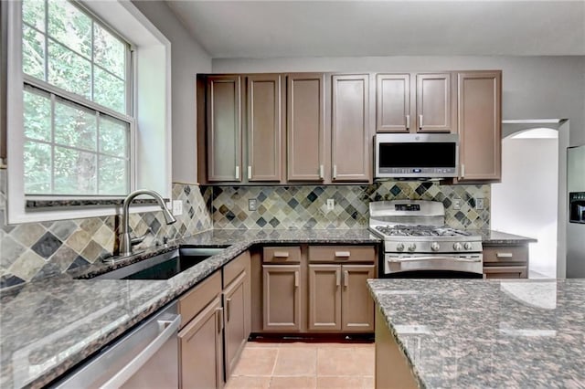 kitchen featuring light tile patterned floors, stainless steel appliances, decorative backsplash, a sink, and dark stone countertops