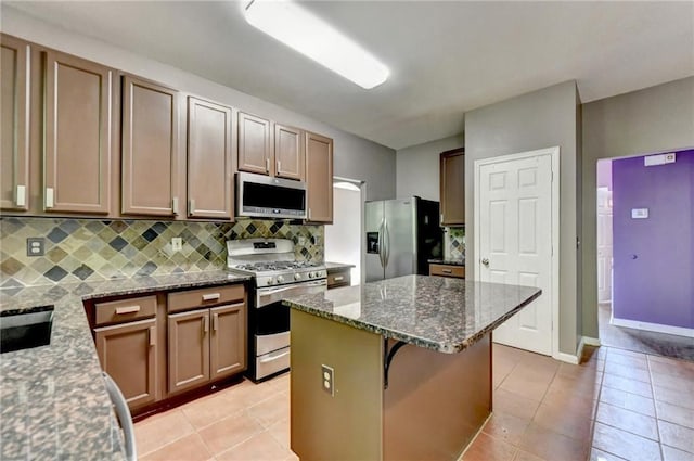 kitchen with appliances with stainless steel finishes, dark stone countertops, a center island, backsplash, and light tile patterned flooring