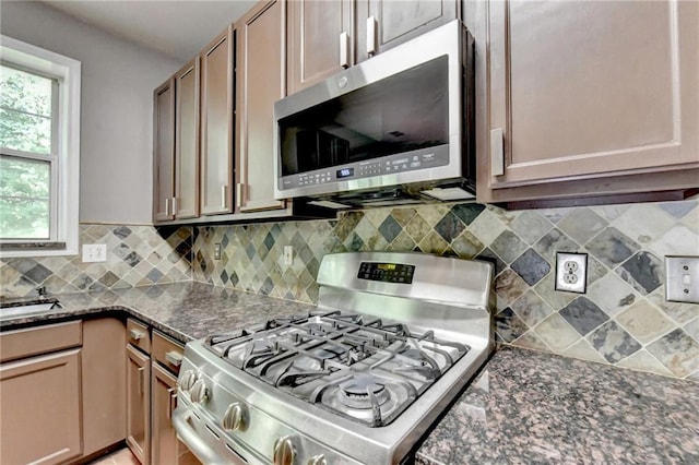 kitchen with stainless steel appliances, dark stone counters, and backsplash