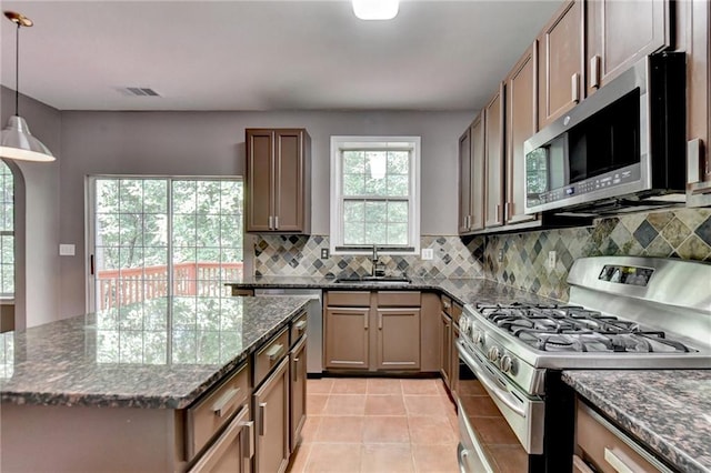 kitchen with dark stone countertops, decorative light fixtures, decorative backsplash, light tile patterned floors, and stainless steel appliances