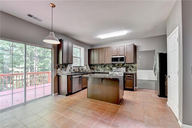 kitchen with stainless steel appliances, decorative light fixtures, tasteful backsplash, light tile patterned floors, and a center island