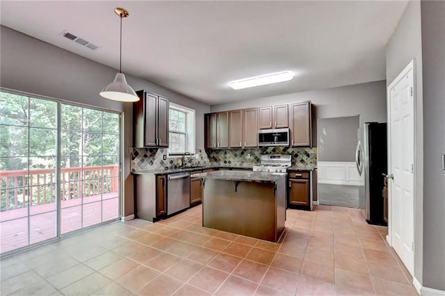 kitchen featuring stainless steel appliances, a sink, visible vents, decorative backsplash, and a center island