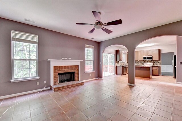 unfurnished living room with ceiling fan, a brick fireplace, and light tile patterned floors