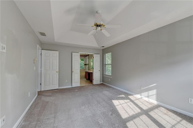 unfurnished bedroom featuring light colored carpet, ensuite bathroom, a tray ceiling, and ceiling fan