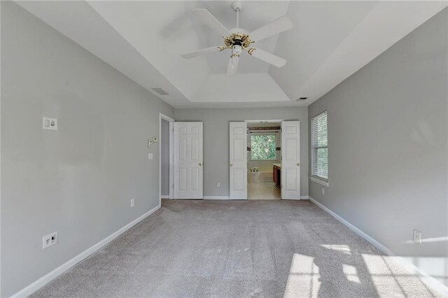 unfurnished bedroom featuring carpet floors, ceiling fan, a raised ceiling, and ensuite bath