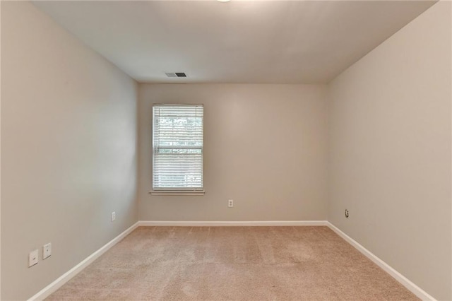 spare room featuring light colored carpet, visible vents, and baseboards