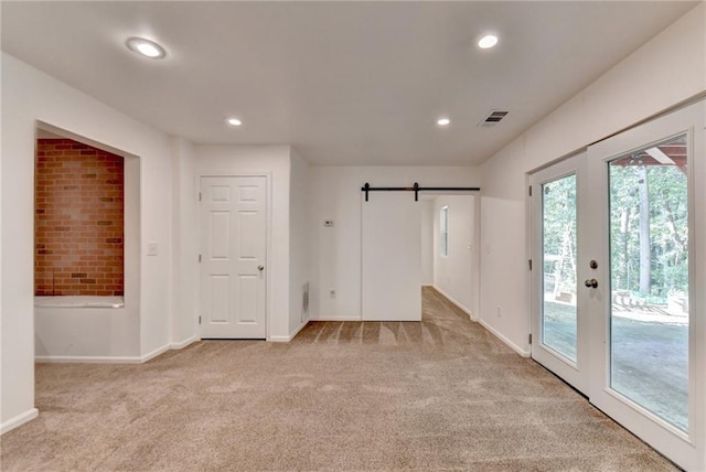 interior space with light colored carpet, french doors, and a barn door