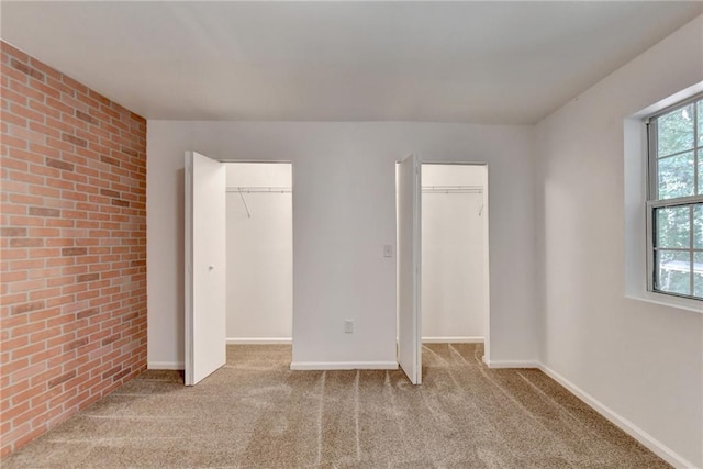 unfurnished bedroom with brick wall, carpet floors, two closets, and baseboards