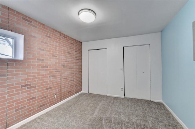 unfurnished bedroom featuring brick wall, two closets, and light carpet