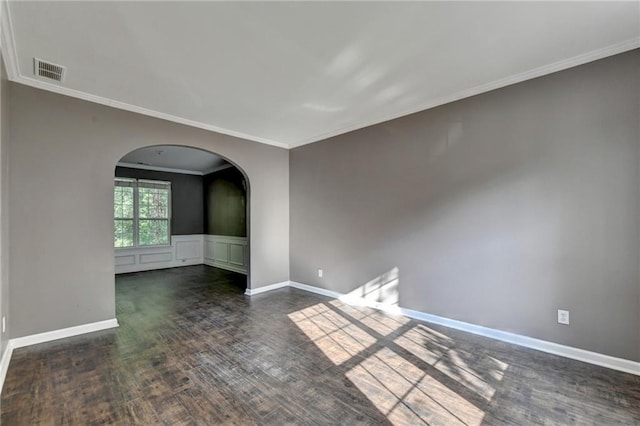 empty room with baseboards, visible vents, arched walkways, wood finished floors, and crown molding