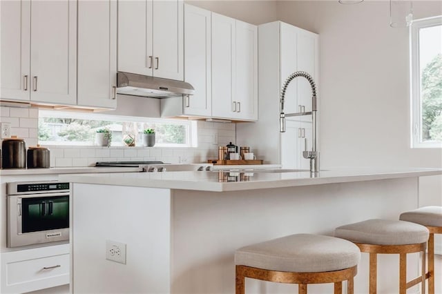 kitchen with a kitchen bar, backsplash, appliances with stainless steel finishes, and white cabinets