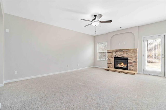 unfurnished living room featuring a stone fireplace, light carpet, and ceiling fan