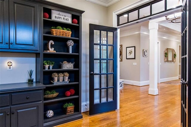 doorway to outside featuring ornate columns, ornamental molding, baseboards, and light wood finished floors