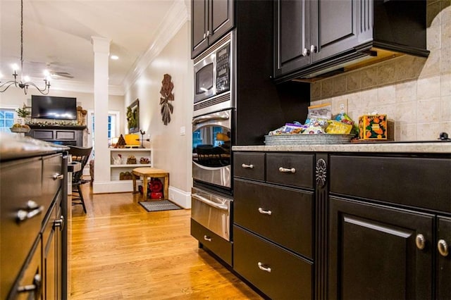 kitchen with crown molding, a warming drawer, appliances with stainless steel finishes, a chandelier, and light wood-style floors