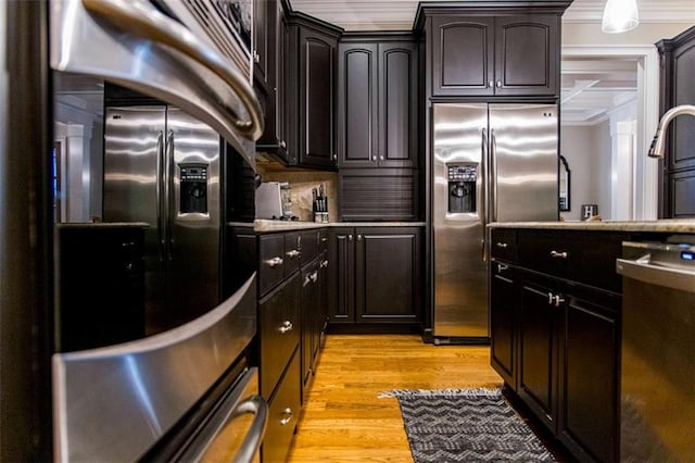 kitchen with stainless steel appliances, ornamental molding, light wood-style flooring, light countertops, and dark brown cabinets