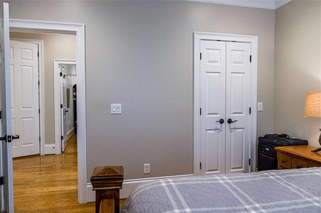 bedroom with wood finished floors, ornamental molding, a closet, and baseboards