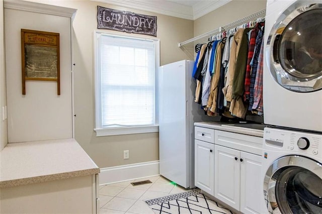 clothes washing area with stacked washing machine and dryer, cabinet space, crown molding, light tile patterned floors, and healthy amount of natural light