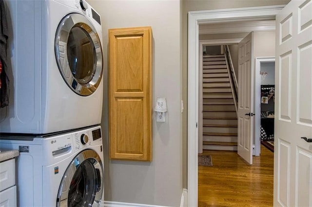 laundry room with cabinet space, stacked washer / dryer, and wood finished floors
