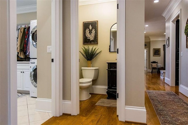 bathroom with stacked washer / drying machine, ornamental molding, toilet, recessed lighting, and wood finished floors