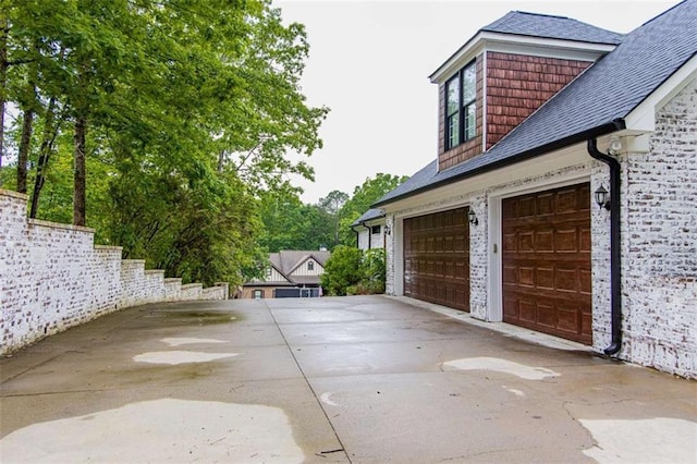 view of side of home featuring an attached garage, roof with shingles, and driveway