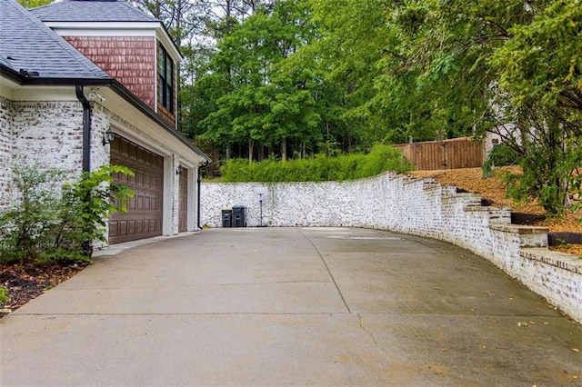 view of property exterior featuring roof with shingles, fence, and a garage