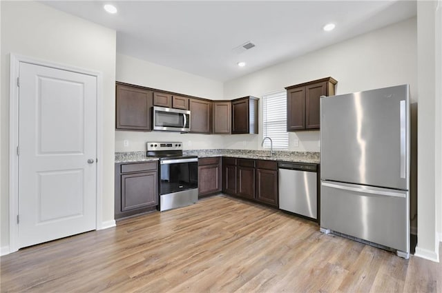 kitchen with stainless steel appliances, light stone countertops, dark brown cabinets, and light hardwood / wood-style flooring