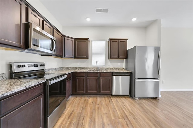 kitchen featuring sink, stainless steel appliances, light stone countertops, dark brown cabinets, and light hardwood / wood-style flooring