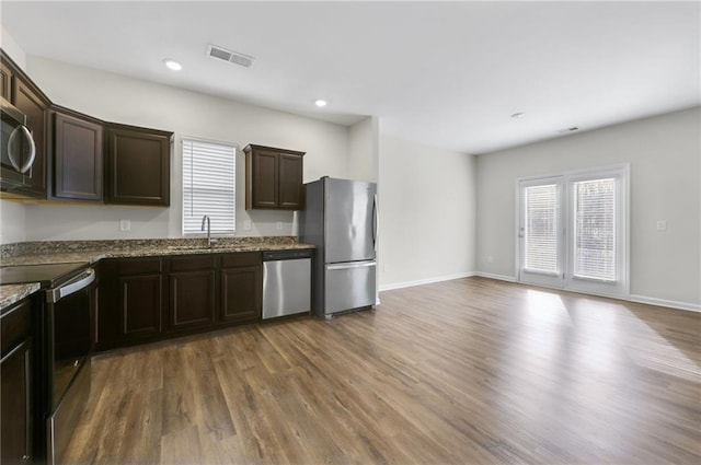 kitchen with dark brown cabinetry, sink, wood-type flooring, dark stone countertops, and appliances with stainless steel finishes