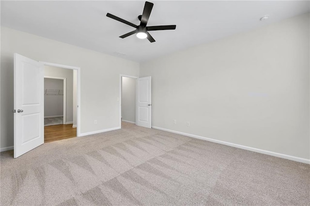 unfurnished bedroom with light carpet, a spacious closet, a closet, and ceiling fan