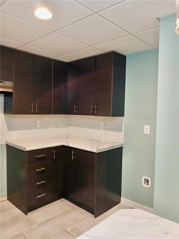 1202 Laurel Cliff Dr SE, Smyrna, GA 30082 - kitchen with light tile patterned flooring, dark brown cabinets, a paneled ceiling, under cabinet range hood, and light stone countertops