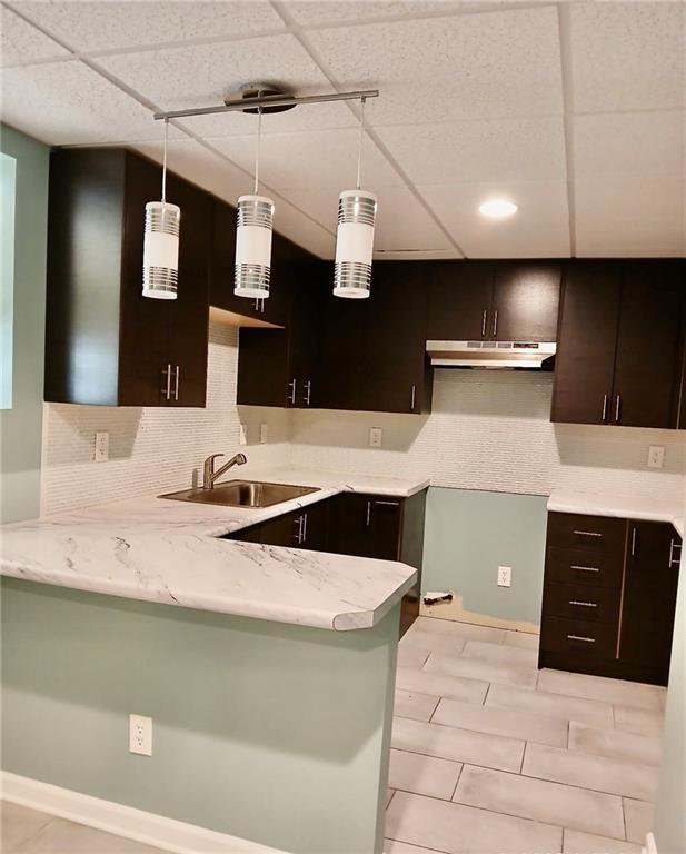 1202 Laurel Cliff Dr SE, Smyrna, GA 30082 - kitchen with a sink, under cabinet range hood, a peninsula, decorative light fixtures, and dark brown cabinets