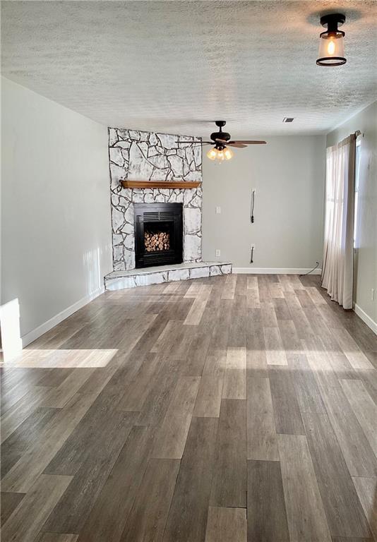 unfurnished living room featuring ceiling fan, a fireplace, a textured ceiling, and hardwood / wood-style flooring