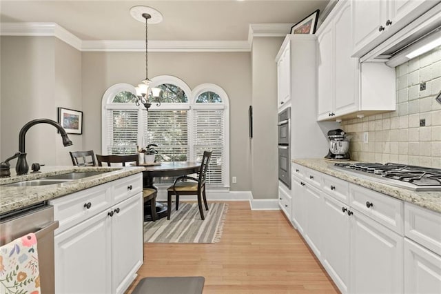kitchen with appliances with stainless steel finishes, a sink, a chandelier, crown molding, and decorative backsplash