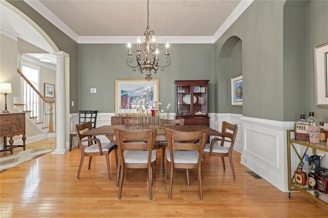 dining room with arched walkways, light wood-style flooring, ornamental molding, stairway, and decorative columns