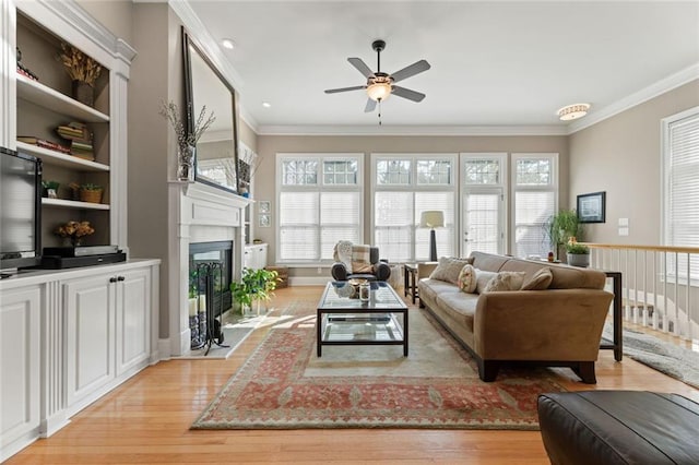 living room featuring a ceiling fan, light wood-type flooring, a fireplace with flush hearth, and ornamental molding