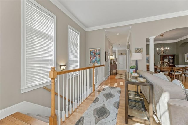 living room with arched walkways, a chandelier, crown molding, light wood-style flooring, and baseboards