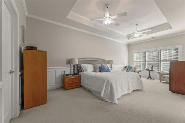 bedroom with a tray ceiling, carpet flooring, crown molding, wainscoting, and a ceiling fan