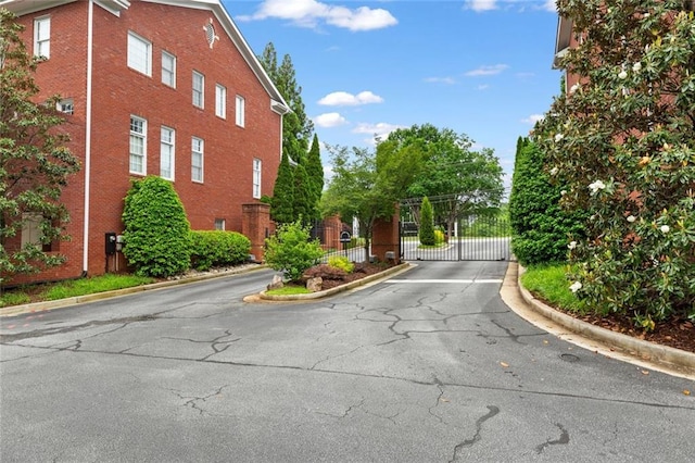 view of asphalt road featuring curbs, a gate, and a gated entry