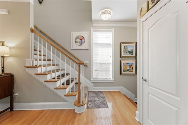 staircase with wood finished floors, baseboards, and crown molding