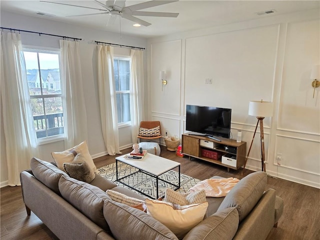 living room with ceiling fan, visible vents, a decorative wall, and wood finished floors