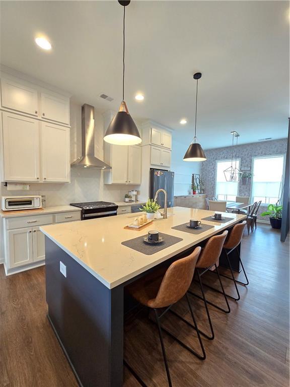 kitchen with fridge, stainless steel range with gas cooktop, white cabinets, wall chimney range hood, and a large island with sink